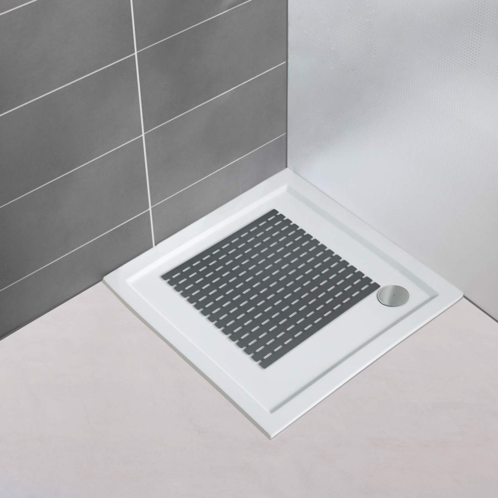 Dark grey plastic, square shower mat in a slatted design in situ on a plain white, square shower tray in the orner of a bathroom with a white floor and one grey tiled wall and one plain white wall