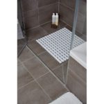 White plastic, square shower mat in a slatted design in situ in a grey, tiled shower enclosure
