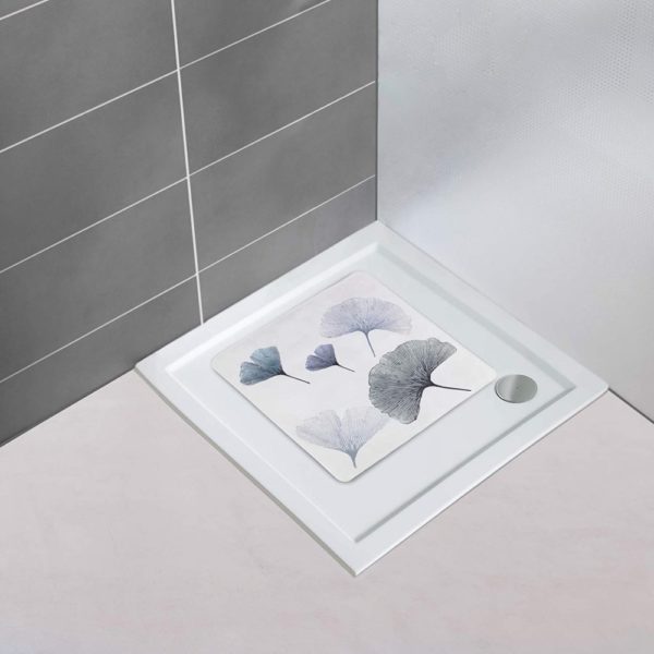 a white, square shower mat multiple , overlapping gingko leaves in varying shades of grey in situ on a plain white, square shower tray in the corner of a bathroom with a white floor and one grey tiled wall and one plain white wall