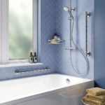 bathroom set up with blue walls and a white bathtub, above this bathtub is a chrome shower on one wall and a large window on the other, to the left of the shower and between the bath and the window are two hand rails to demonstrate possible positions for it