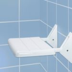 white rectangular shower seat on a blue tiled wall. it is folded in the down position