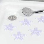 five purple and white, starfish shaped anti-slip stickers arranged by the drain on a white shower tray, a chrome showerhead is placed above them
