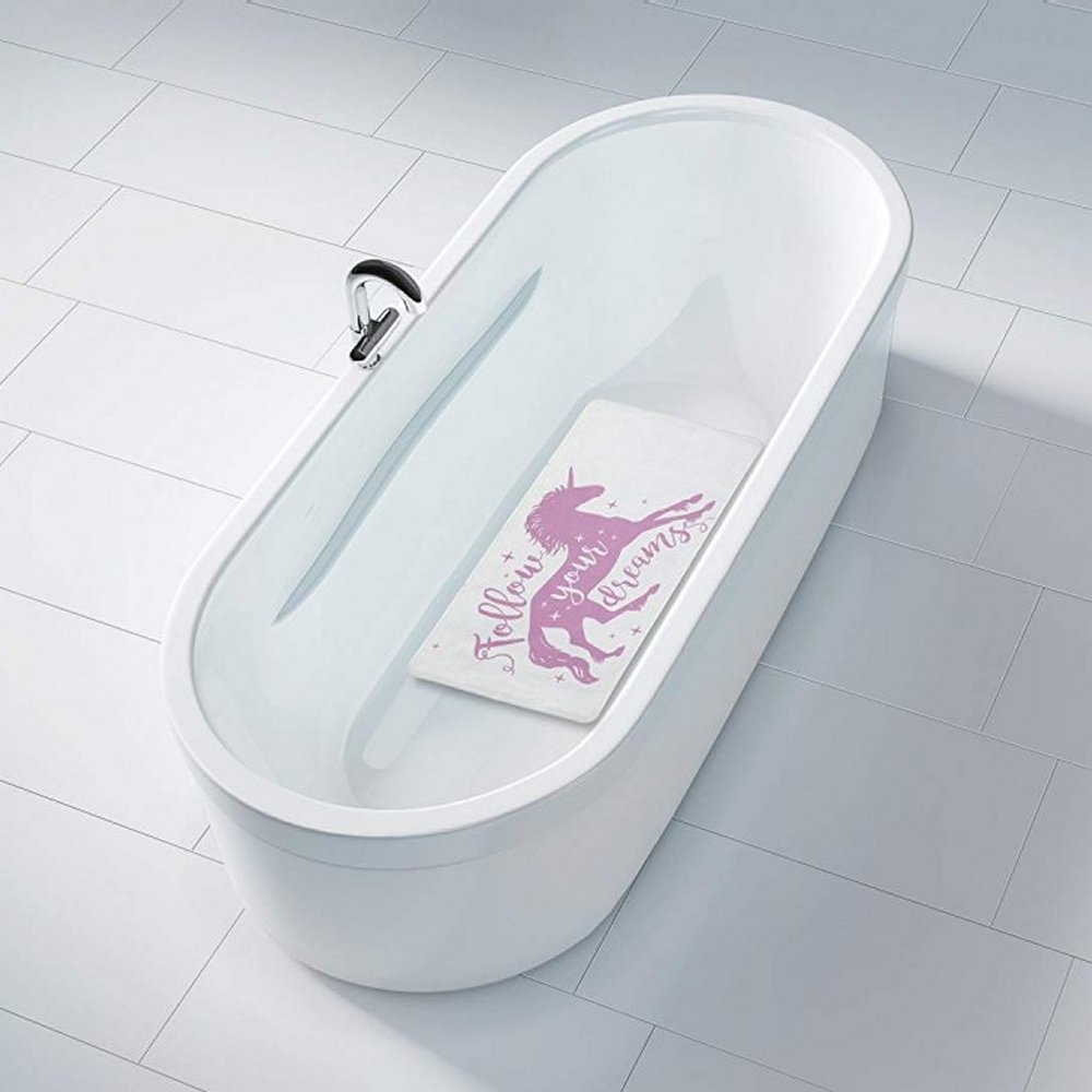 White rectangular bath mat with a pink silohuette of a unicorn surrounded with pink sparkles. In a fanciful font, it reads "Follow Your Dreams" also in pink exept for the word "your" which overlays the unicorn and is in white. It is centred in a white bathtub