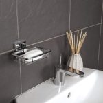 chrome, wall mounted soap basket with square wall plate on a grey tiled wall above a white sink with a reed diffuser