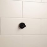 round, matt black single robe hook on a white tiled wall