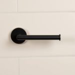 matt black roll holder, it is bar shaped and attaches to the wall on one nd with a round back plate. it is on a white, tiled wall