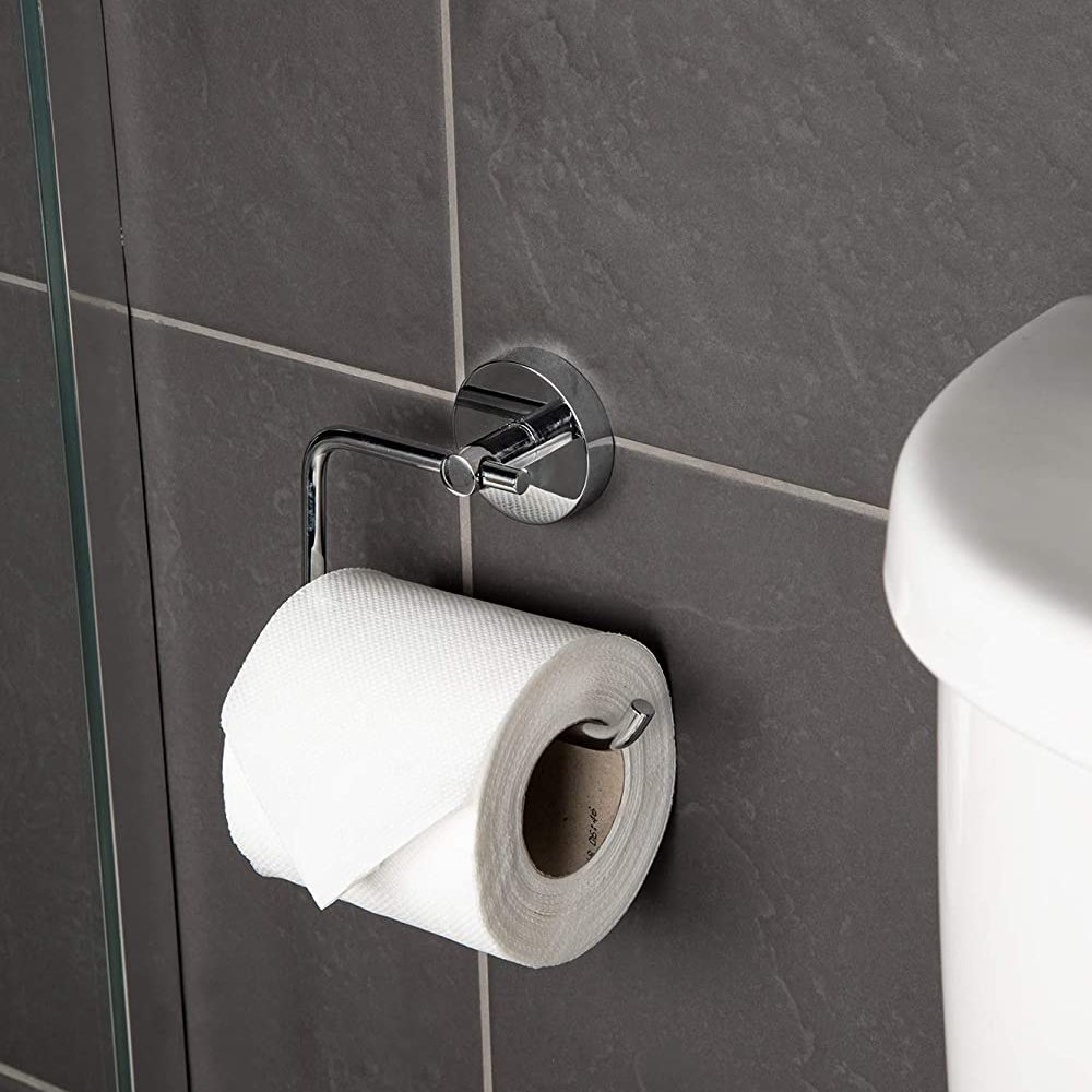 chrome toilet roll holder with circular wall mount, the holder is a rectangular hook shape with rounded corners.. it is on a grey tiled wall by a white cistern and is holding a white roll of toilet paper.