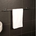 chrome towel rail with round wall brackets on each end it is mounted on a dark grey tiled wall nd is holding a white towel